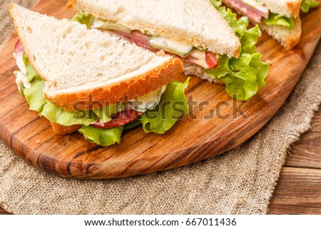 Photo of fresh sandwiches on wooden board at canvas fabric