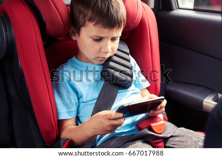 Mid shot of gloomy boy playing in phone while sitting in baby seat