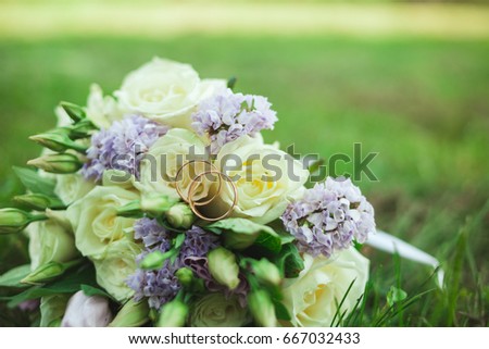 Beautiful bridal bouquet of bride on green grass with gold rings.