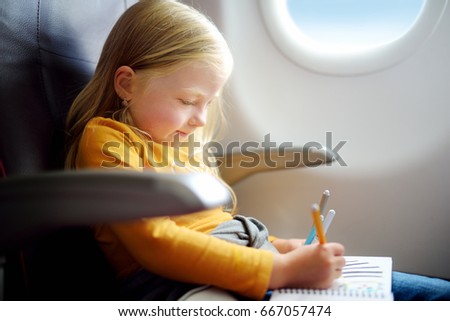 Adorable little girl traveling by an airplane. Child sitting by aircraft window and drawing a picture with colorful felt-tip pens.