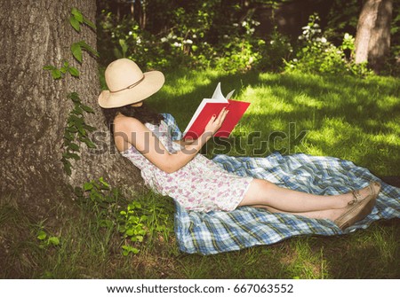 Woman relaxing on a tree reading a book outside in the grass