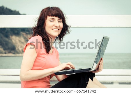 Vintage photo, Happy smiling woman sitting on bench by seaside with her laptop, using computer concept