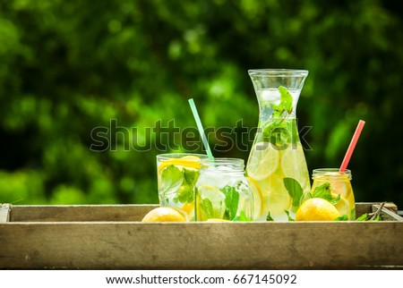 Delicious homemade lemonade in graphene and jars with mint and lemons on the blurred background of greenery