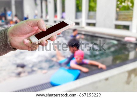 Man use mobile phone, blur images of teaching children to swim as background.
