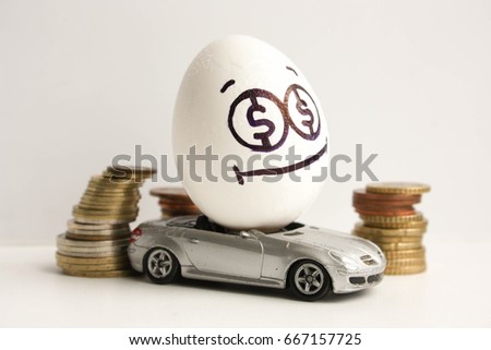 Business concept. Business car. A happy egg with a painted face and a sticky tongue in the middle of a pile of coins. Egg on a gray car. Photo for your design
