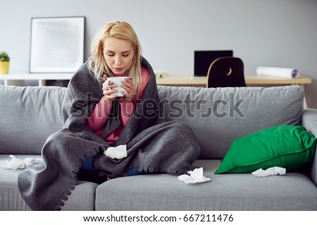 Young sick woman sitting on sofa drinking tea Royalty-Free Stock Photo #667211476