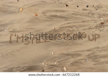 Handwriting  words "I'M STILL LOOKING UP." on sand of beach.