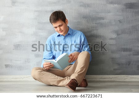 Young man reading book on grey wall background
