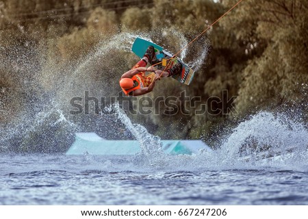 Man makes an extreme jump on wakeboarding, around there are a lot of splashes and splashes of water. This is an extreme sport. Royalty-Free Stock Photo #667247206