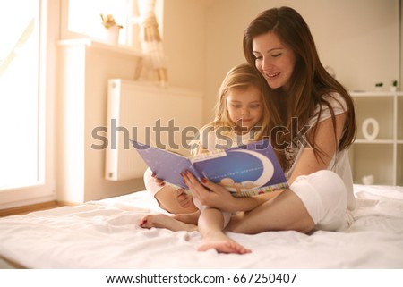 Mother reading her daughter the story after waking up. Mother with her daughter enjoying in the story.