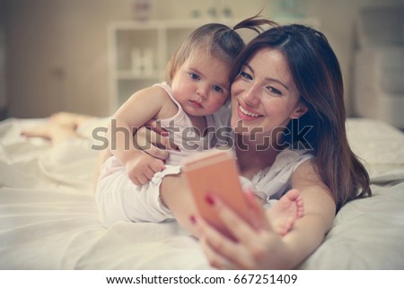 Mother with her little baby having fun in the bed. Mother making self-picture with her cute little baby in the bed.