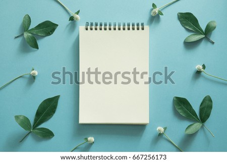 blank notepad with flower and leaf on blue background.