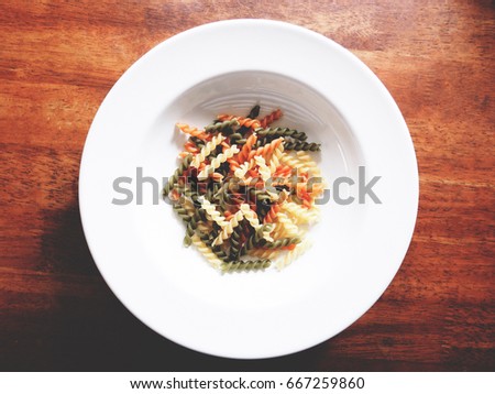 It's time to cook, The picture of multicolored of dried fusilli consist of yellow, orange and green on white plate above wooden table.  soft tone color