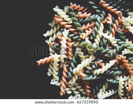 It's time for Italian menu, The picture of multicolored of dried fusilli consist of yellow, orange and green on black background.  soft tone color
