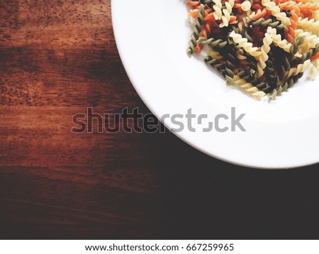 It's time to cook, The picture of multicolored of dried fusilli consist of yellow, orange and green on white plate above wooden table. selective focus,  soft tone color