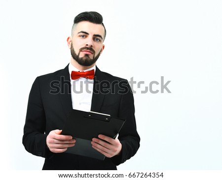 Stylish presenter with beard and confident face expression in classic black suit and red bow tie holding black clip folder, isolated on white background. Concept of presentation and report