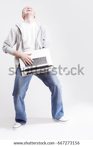 Youth Lifestyle Concepts and Ideas. Full Length Portrait of Expressive Caucasian Man Wearing Hoodie and Blue Jeans Posing with Laptop on Hands Against White Background. Vertical Image Composition