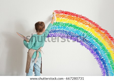 Childhood concept. Little painter drawing rainbow on white wall background