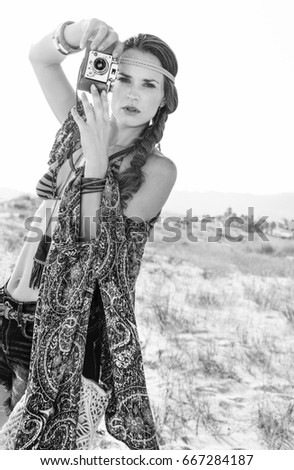 Bohemian vibe vacation. trendy hipster in jeans shorts and cape outdoors in the summer evening holding retro photo camera