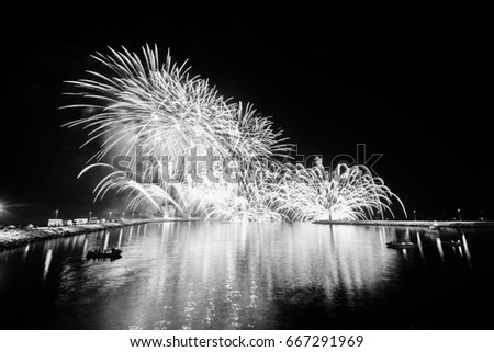 Fireworks in a harbor with boats illuminated by reflections on the water