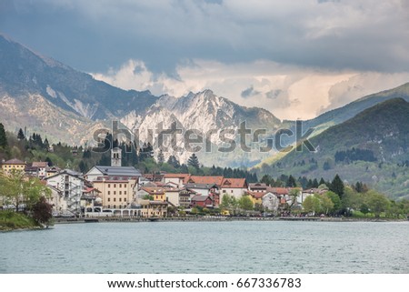 view of the Barcis city on the lakeside surrounding mountains against a dramatic cloudy blue sky background in Valcellina, Pordenone, Italy
