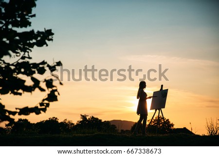 Silhouette of a girl. The blonde girl paints a painting on the canvas with the help of paints.