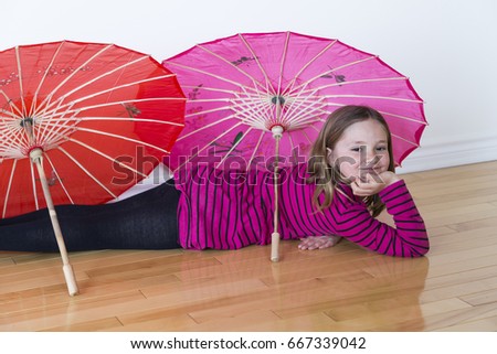 Six-year old little girl lying down on floor with painted silk sun umbrellas