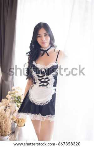Beautiful Maid or housemaid or maidservant or housekeeper with maid uniform or cosplay maid standing beside the window looking to the camera (a little bit over exposure from lighting outside window)
