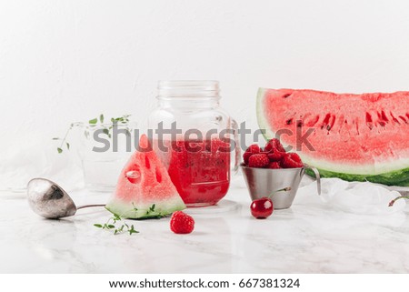 Glass jar cup with refreshing watermelon and strawberry lemonade with lime juice, ginger and honey on marble table and white background. Summertime beverage concept. Copy space