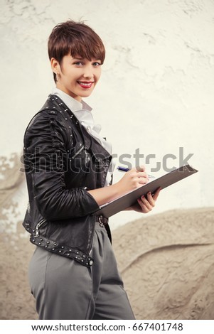 Happy young business woman with clipboard. Stylish fashion female model in black leather jacket 