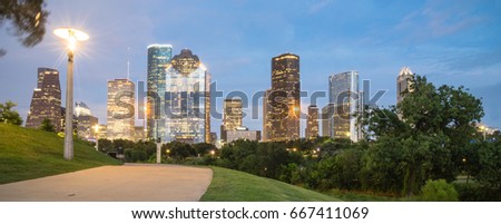Downtown Houston illuminated at blue hour with pathway, green park lawn and modern skylines light in background. View from Eleanor Park along Bayou River. Architecture and travel concept. Panorama.