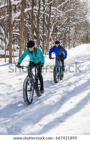 An attractive couple rides their fat bikes on a trail in the snow.