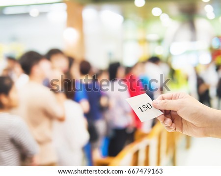 Male hand holding queue card over long line waiting people Royalty-Free Stock Photo #667479163
