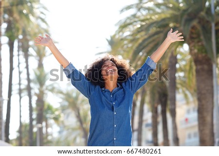 Portrait of happy carefree woman with arms outstretched outside 