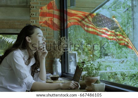 Happy young half Thai-American woman in relax moment sit and facing against window over background of the American flag blowing in the wind.