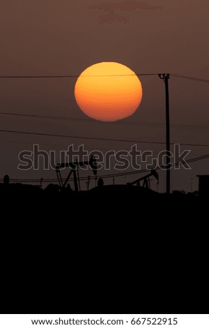 Silhouette of crude oil pump in oilfield at sunset golden hour