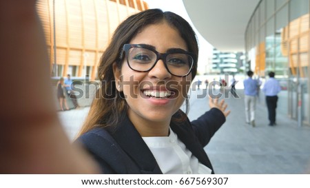 Portrait of a young beautiful business woman (student) in a suit, glasses, walking through the city, video call, selfie, holding a phone. Concept: new business, communication, Arab, banker, manager. Royalty-Free Stock Photo #667569307
