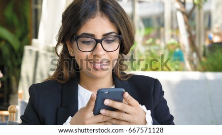 Portrait of a young beautiful business woman (student) in a suit, glasses, sitting at the table, talking on the phone, writing a message. Concept: new business, communication, Arab, banker, manager.