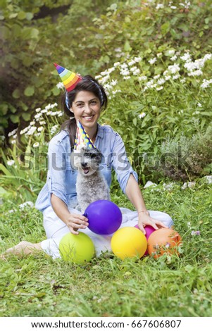 happy young  woman celebrating birthday with her dog ,balloons and hats in a summer garden