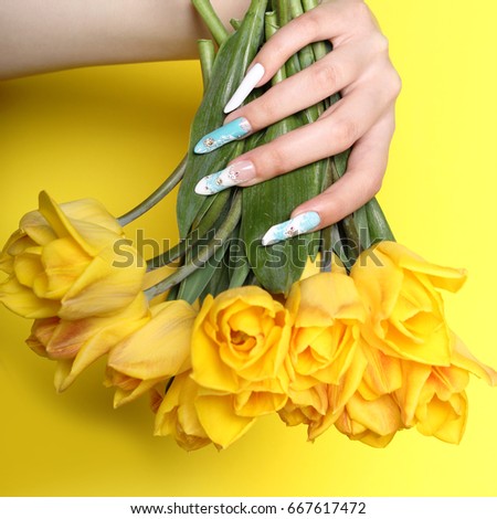 Stylish trendy female manicure. Tulips flower in beautiful young woman's hands. Yellow background. Nail Polish. Art Manicure. Multi-colored Nail Polish. Beauty hands. Stylish Colorful Nails