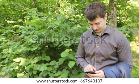 Happy man in black suit typing sms on smartphone in the forest.