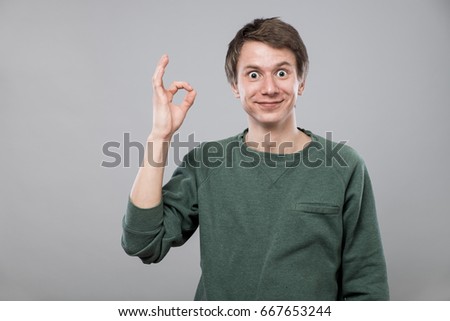Smiling young man with ok sign on grey background