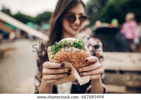 tasty burger. stylish hipster woman holding juicy hamburger in hands close up. boho girl with hamburger at street food festival. summertime. summer vacation picnic. space for text 