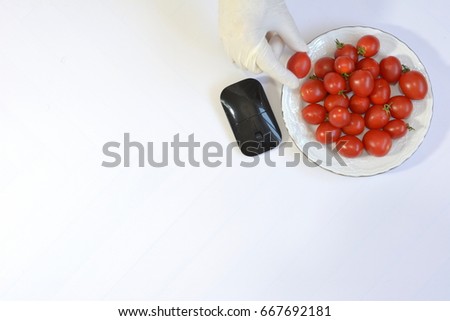 A scientist with white gloves picks one of the red tomatoes next to a black mouse