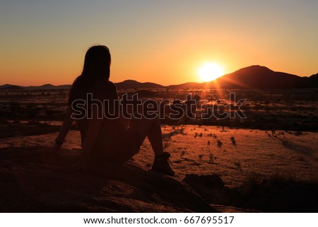Lonely girl watching the sunset at african savanna landscape. Namibia, South of Africa.