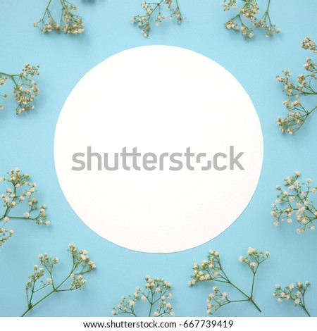 Creative layout made of flowers with paper card note on blue background. Flat lay. Nature concept