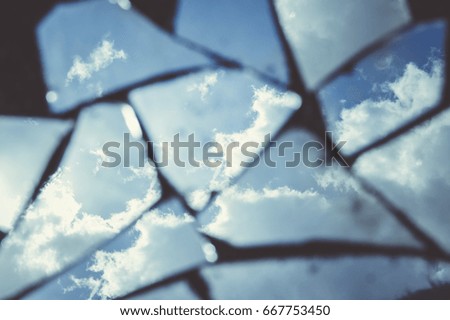 Reflection of a blue sky with fluffy clouds in dirty broken pieces of a mirror. Tinted stylish photo.