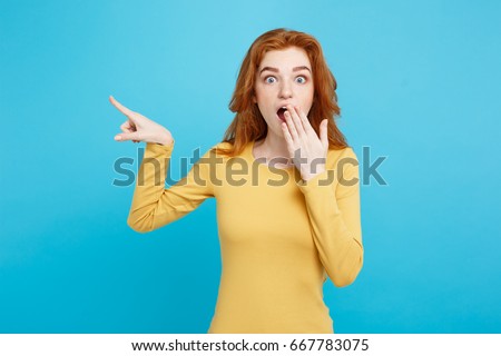 Close up Portrait young beautiful attractive redhair girl with shocking with something and pointing finger. Blue Pastel Background. Copy space. Royalty-Free Stock Photo #667783075
