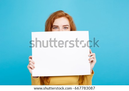 Close up Portrait young beautiful attractive redhair girl smiling showing blank sign. Blue Pastel Background. Copy space.