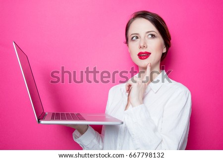 Portrait of young red-haired businesswoman with laptop on pink background